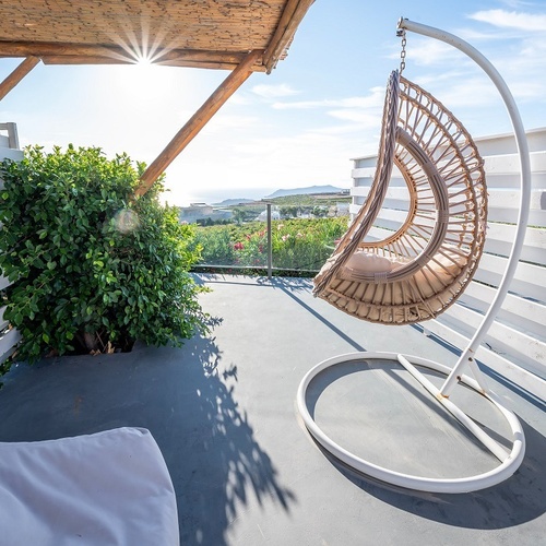 a hanging chair on a balcony with the sun shining through the fence