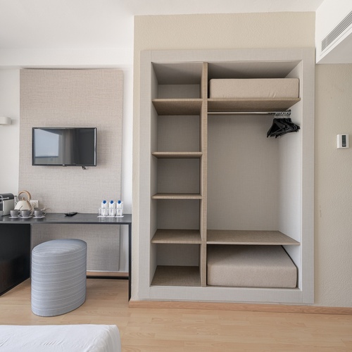 Quarto de hotel com TV, minibar e armário aberto. Smy: Corporativa.