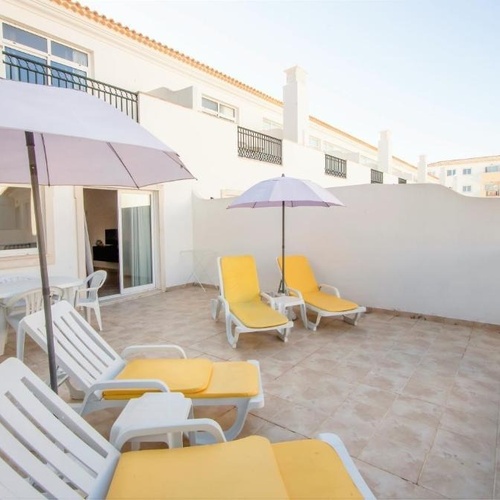 a patio with chairs and an umbrella in front of a white building