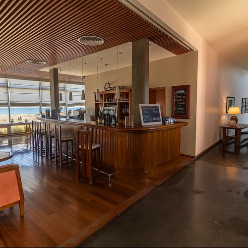 Un'elegante area bar con vista mare attraverso ampie finestre, pavimento in legno e un corridoio ben illuminato adiacente.