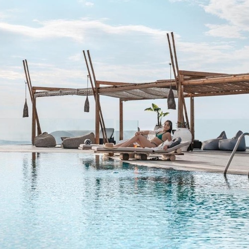 a woman in a bikini sits on a lounge chair near a swimming pool