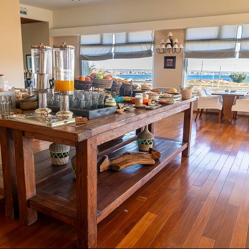 Un tavolo da buffet per la colazione è allestito in una sala luminosa con ampie finestre che offrono una vista sul mare.