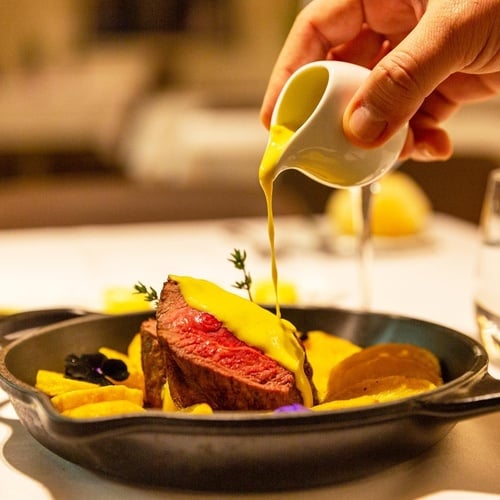 a person pouring sauce on a steak in a skillet