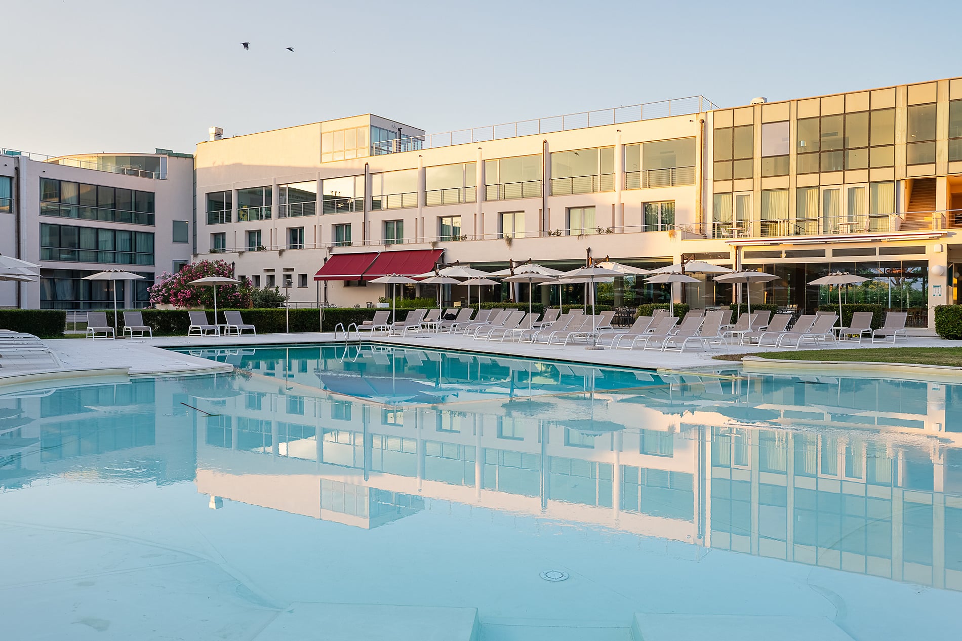 Hôtel Pisa Plaza 5* | Site officiel : Façade moderne avec jardin fleuri et bateau historique.