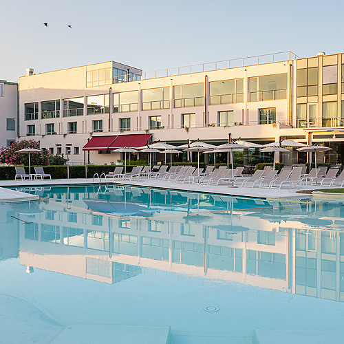 Piscine d'un hôtel de luxe avec chaises longues et parasols, reflétant le bâtiment Smy: Corporativa.