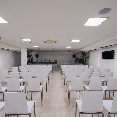 Salle de conférence blanche avec rangées de chaises, projecteur et écran. Idéal pour Smy: Corporativa.