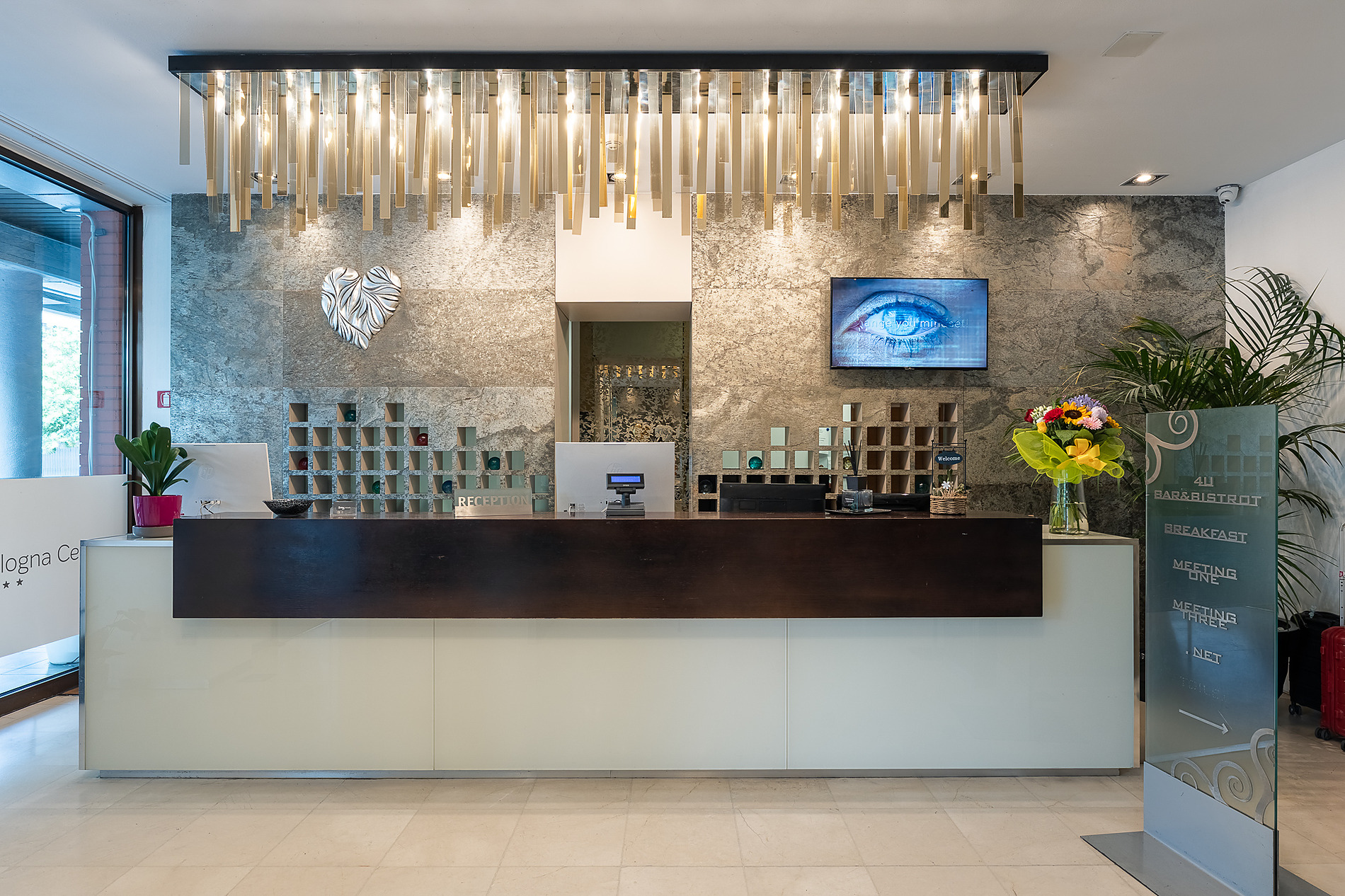 Moderno lobby hotel Smy Bologna Centrale 4 estrellas con orquídeas y sofás blancos.