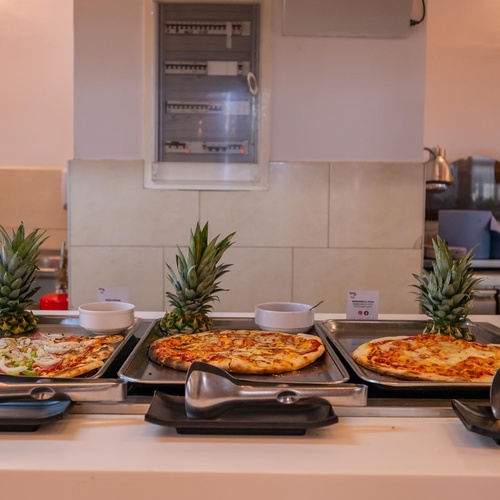 three pizzas are on trays with pineapples in the background