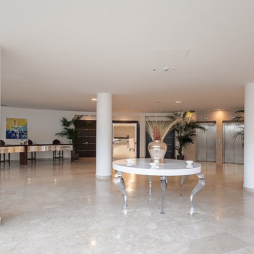 Réception moderne de l'hôtel avec table blanche et plantes vertes, près des ascenseurs. Idéal pour Smy: Corporativa.