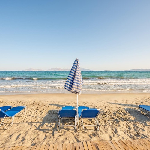 blue chairs and umbrellas on a beach with the ocean in the background
