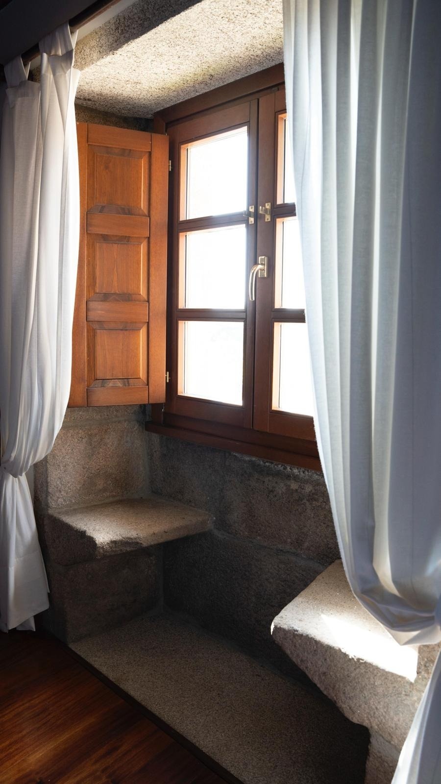 una ventana con persianas de madera y cortinas blancas