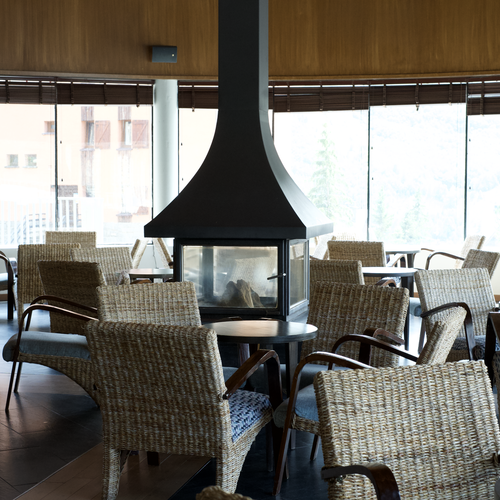 Acogedor salón de hotel con chimenea, sillas de mimbre y grandes ventanales con vistas.