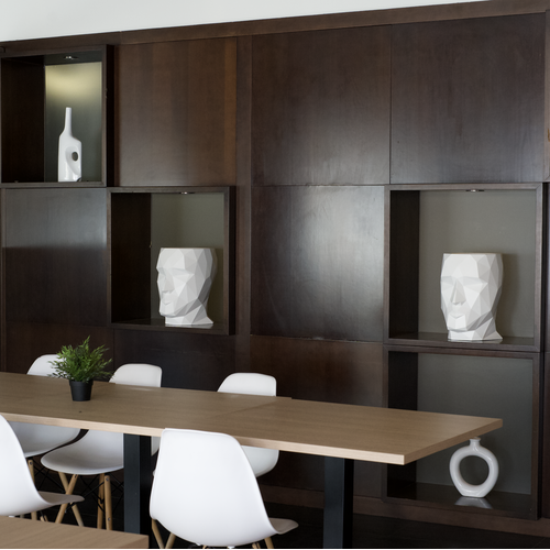 Sala de reuniones moderna en hotel con mesa de madera clara, sillas blancas y estanterías decoradas.