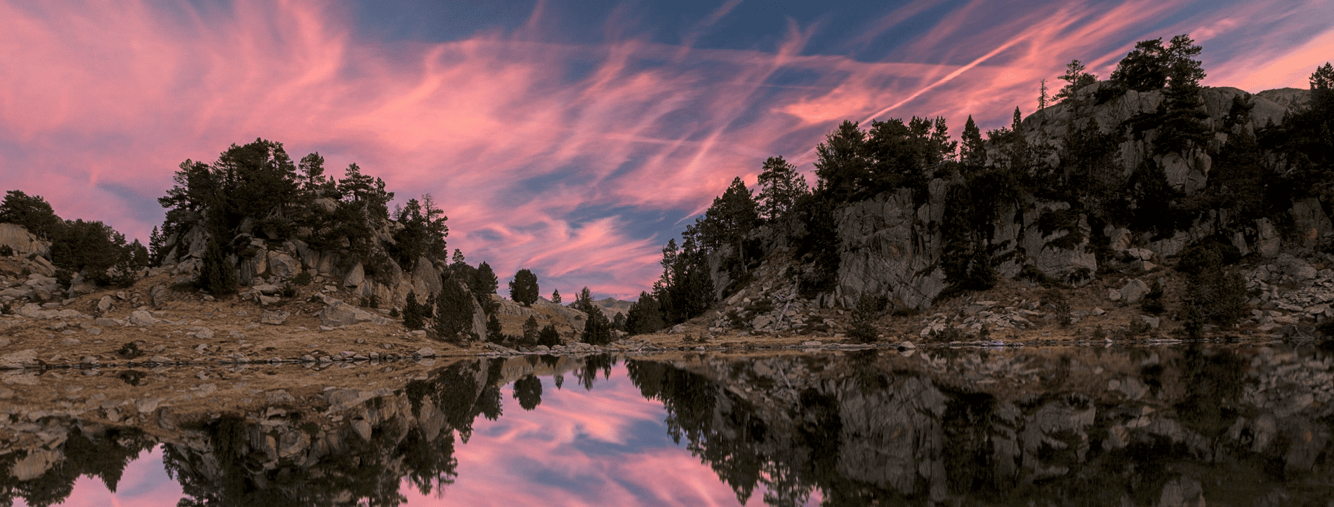 una puesta de sol rosa se refleja en un lago rodeado de montañas