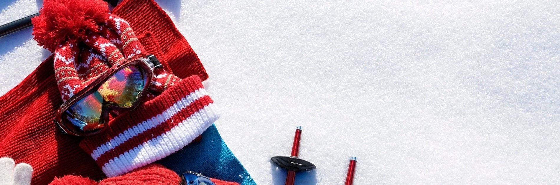 un sombrero rojo , gafas , guantes y esquís están en la nieve