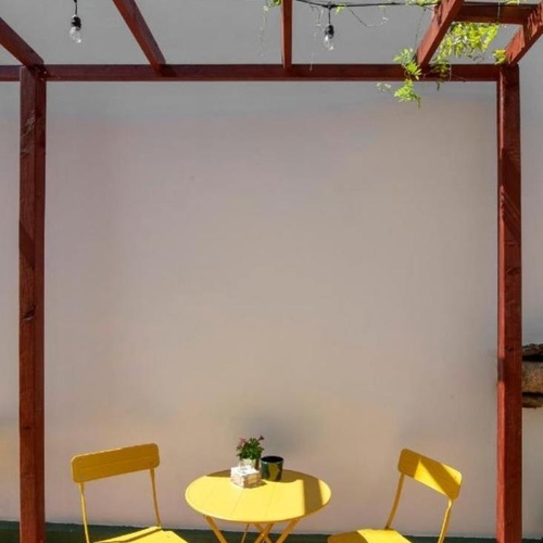 una mesa y dos sillas amarillas están bajo una pérgola de madera