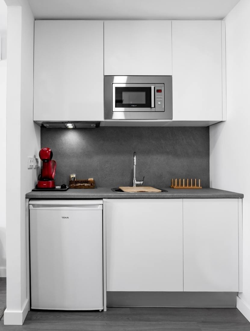 una pequeña cocina con gabinetes blancos y electrodomésticos de teka