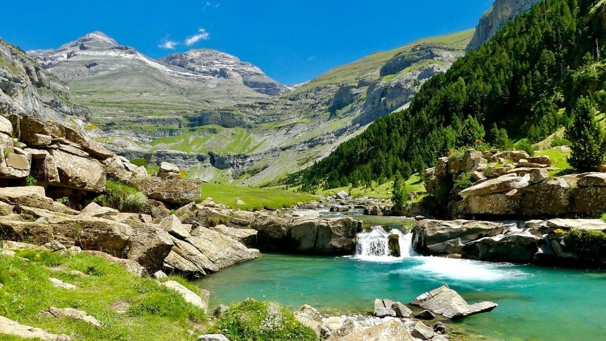 un río que fluye a través de un valle con montañas en el fondo