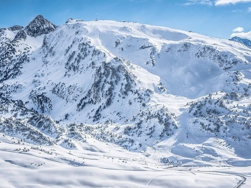 a snowy mountain covered in trees with a blue sky in the background