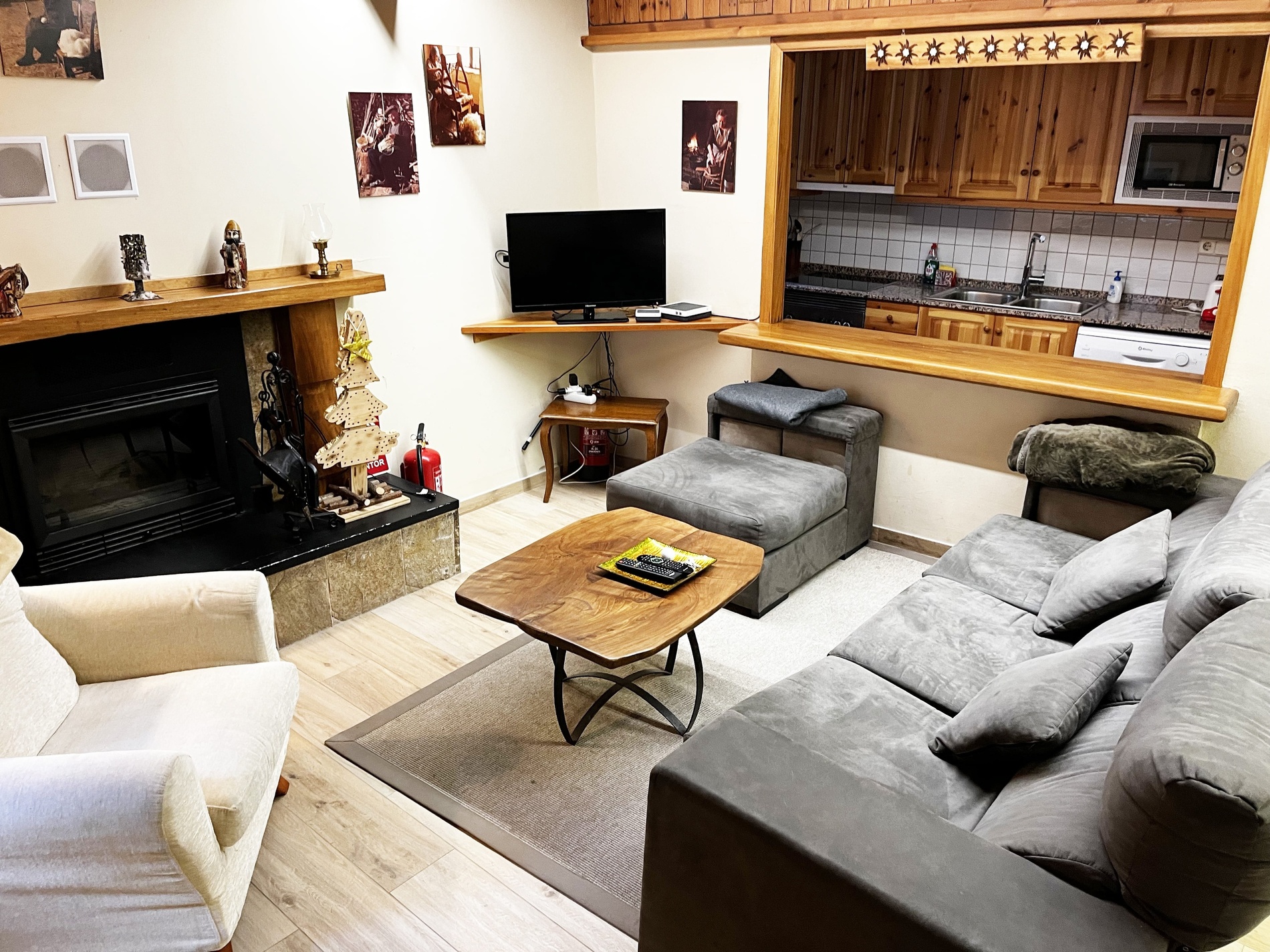 Ce salon-cuisine, aménagé dans un style chaleureux et rustique, est équipé d'une cheminée, d'un grand canapé gris et d'une télévision.