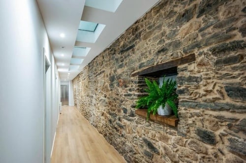 a long hallway with a stone wall and a window with a plant in it
