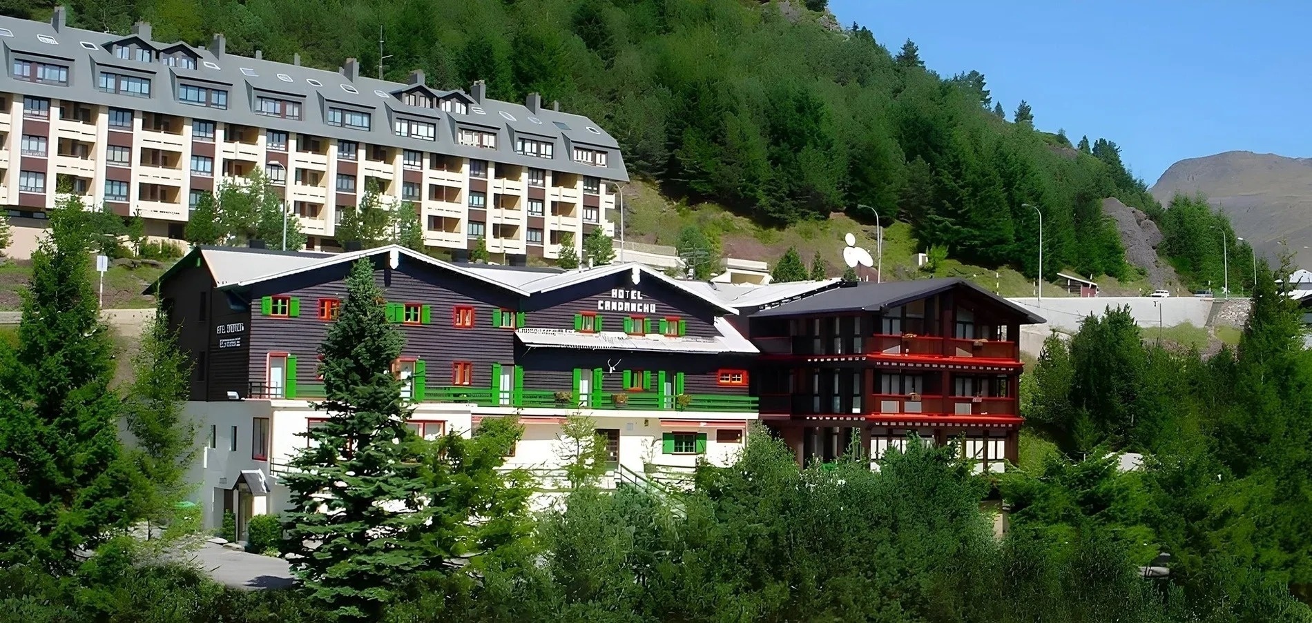 un hotel con balcones verdes y rojos está rodeado de árboles