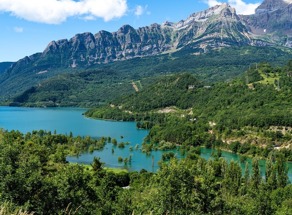 a lake surrounded by mountains and trees on a sunny day