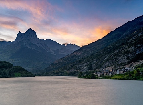 un lago rodeado de montañas al atardecer con un pueblo en la orilla