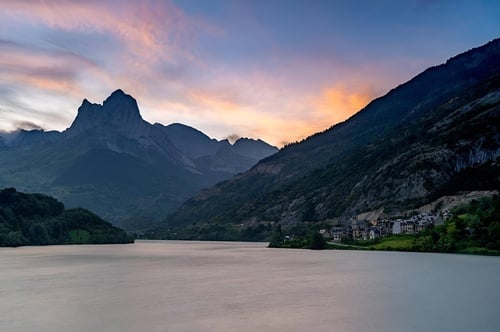 un lago rodeado de montañas al atardecer con un pueblo en la orilla