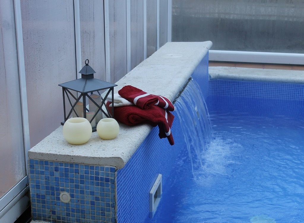 une lanterne et des bougies sont assises à côté d' une chute d' eau dans une piscine