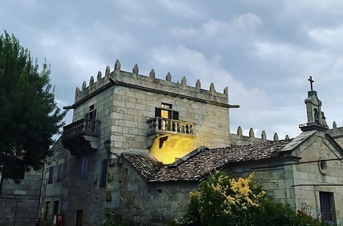 un edificio de piedra con un balcón y una iglesia al fondo