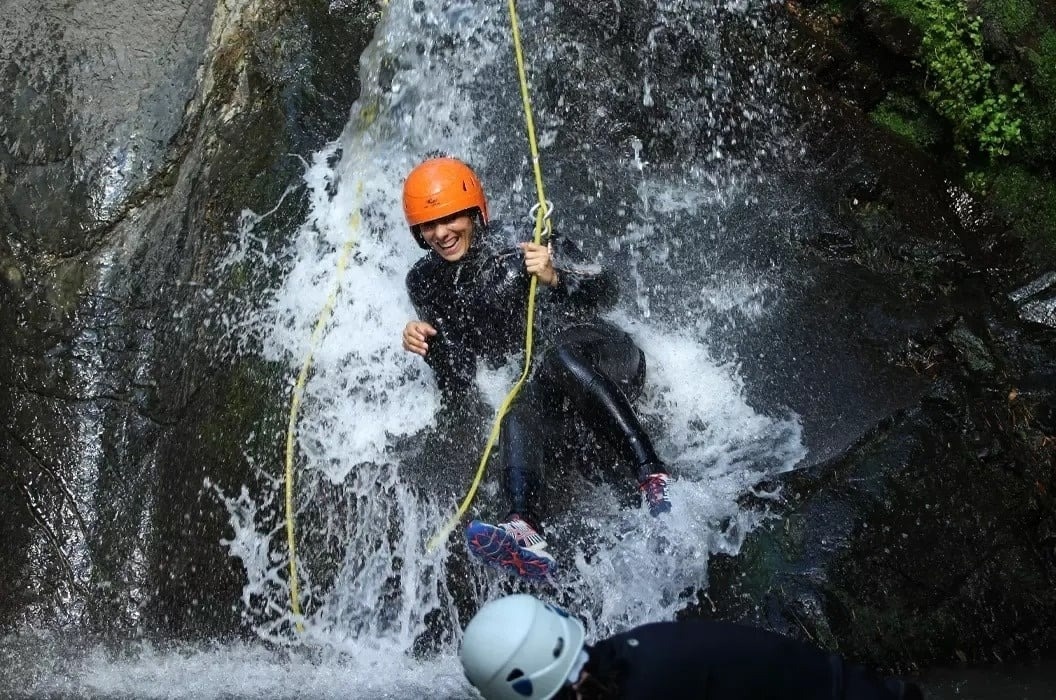 Mujer sonriendo haciendo barranquismo por cascada, con traje de neopreno y casco.