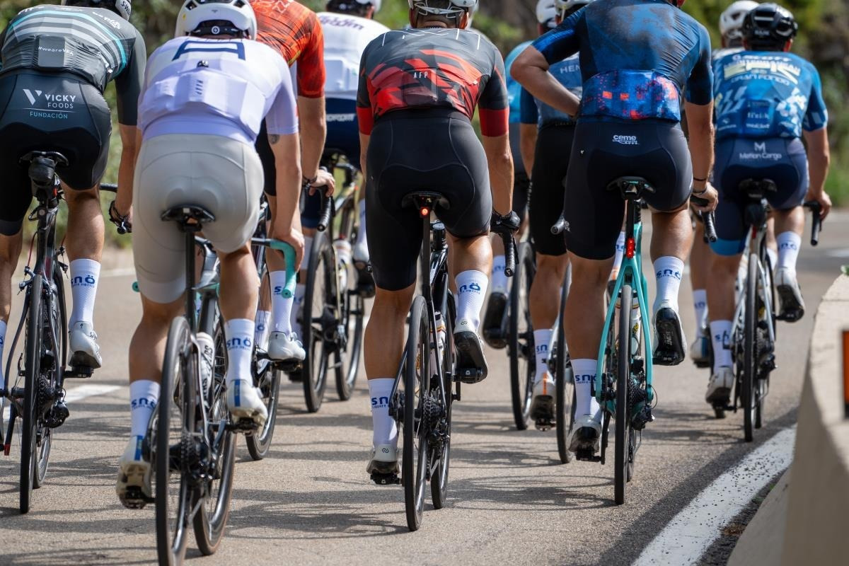 Ciclistas compiten en una carrera con SNO: Corporativa en el jersey.