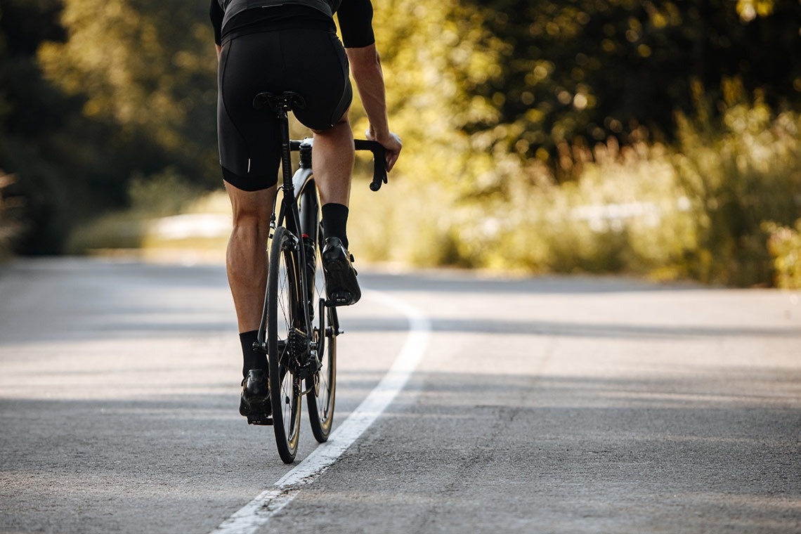 un homme fait du vélo sur une route avec des arbres en arrière-plan