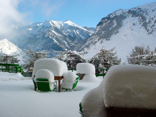 snow covered chairs and a table with mountains in the background