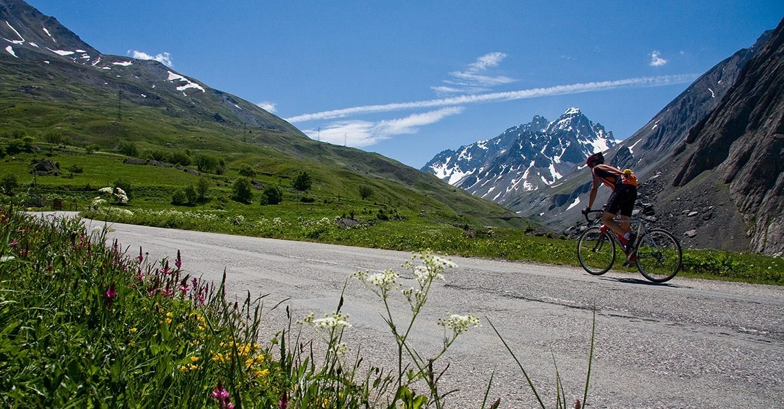un hombre monta una bicicleta por una carretera con montañas en el fondo