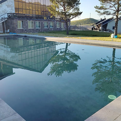 Piscina de hotel con reflejo de edificio y árboles, perfecta para SNO: La Corza Blanca.
