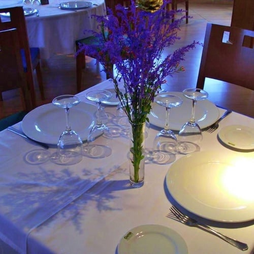 una mesa con platos y copas y un jarrón de flores moradas