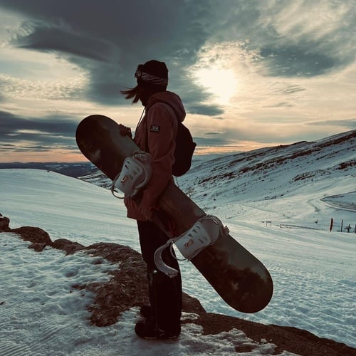 SNO: La Corza Blanca, snowboarder admirando la puesta de sol en la montaña.