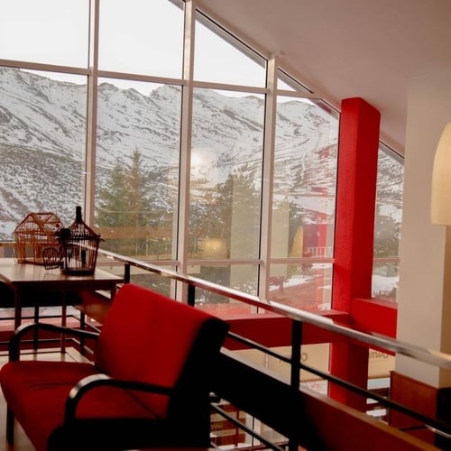 un banco rojo está junto a una ventana con una vista de las montañas en el fondo