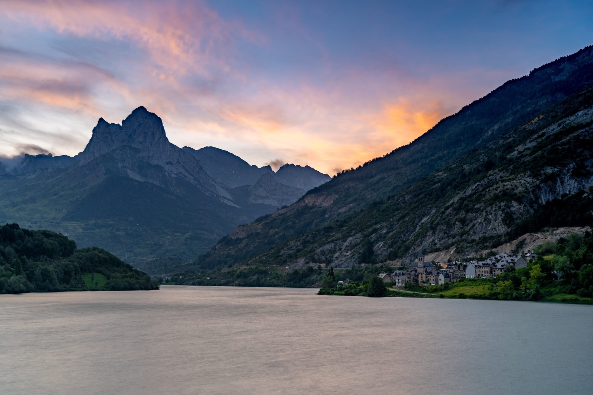 un lago con montañas en el fondo y flores moradas en primer plano