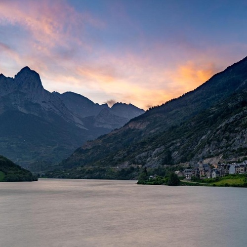 un lago rodeado de montañas al atardecer con un pueblo en la orilla