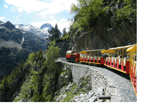 un train rouge et jaune traverse une vallée avec des montagnes en arrière-plan