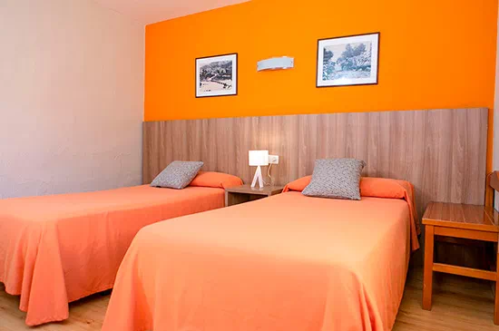 una habitación con dos camas , dos mesitas de noche y una pared naranja .