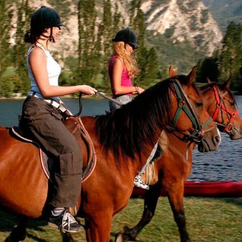 dos mujeres montan a caballo junto a un lago