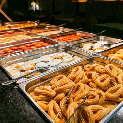 un buffet lleno de comida incluyendo churros y huevos fritos