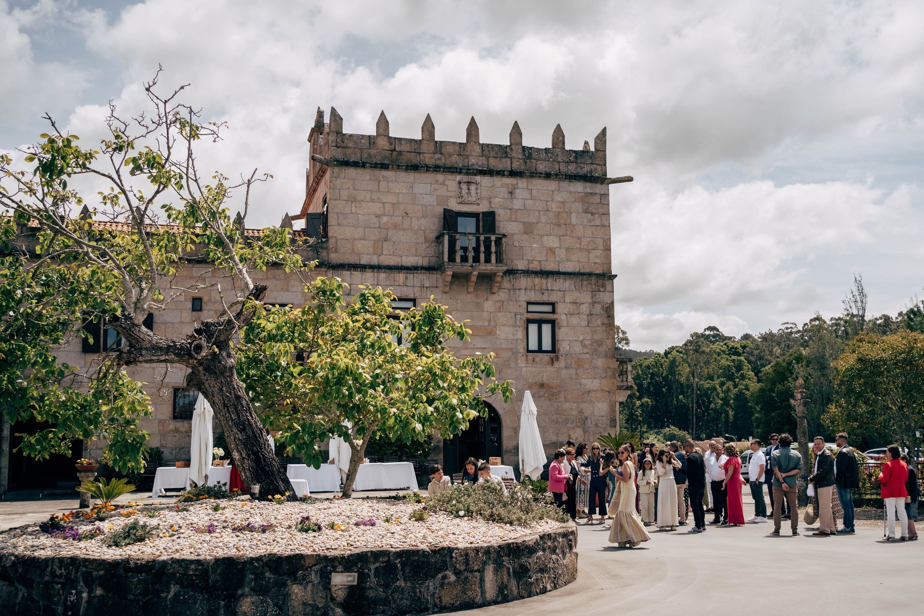 una niña con un vestido blanco y una corona de flores está rezando en una ventana .