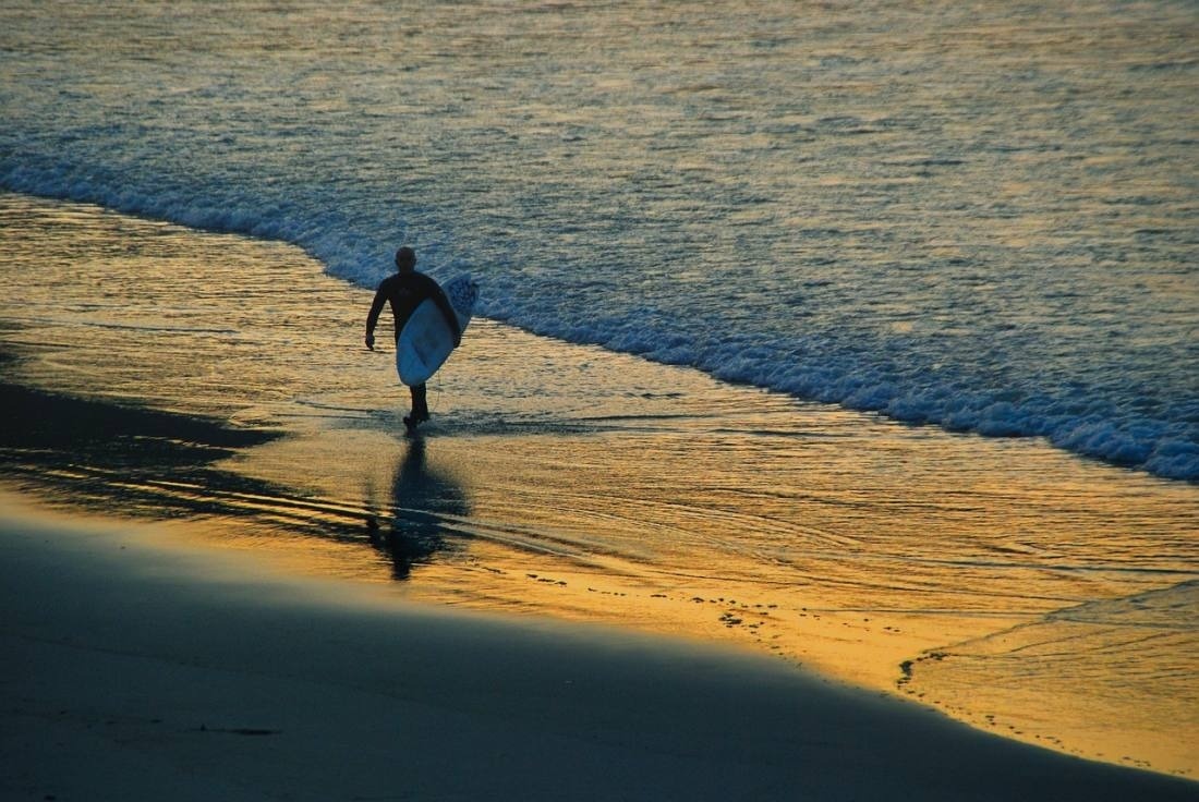 un hombre lleva una tabla de surf por la playa al atardecer