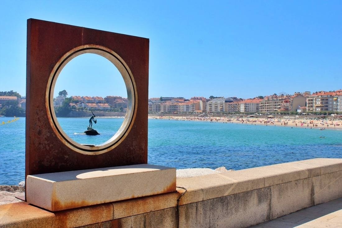 una estatua de una mujer en una isla en el océano se ve a través de un marco de metal oxidado