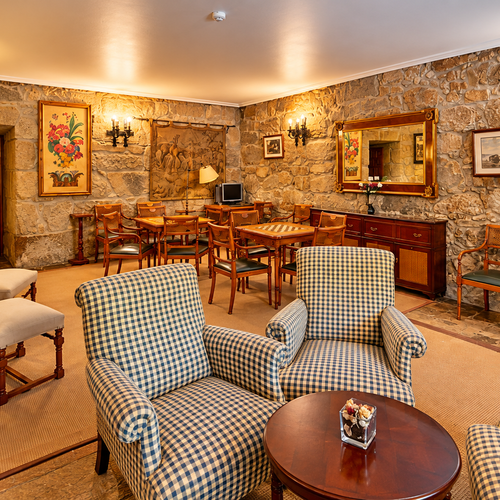Salon confortable du SNO: Pazo O Rial avec fauteuils à carreaux et murs en pierre.